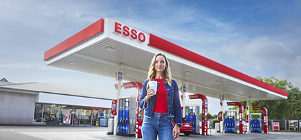Frau hält einen Becher in einer Esso-Tankstelle.